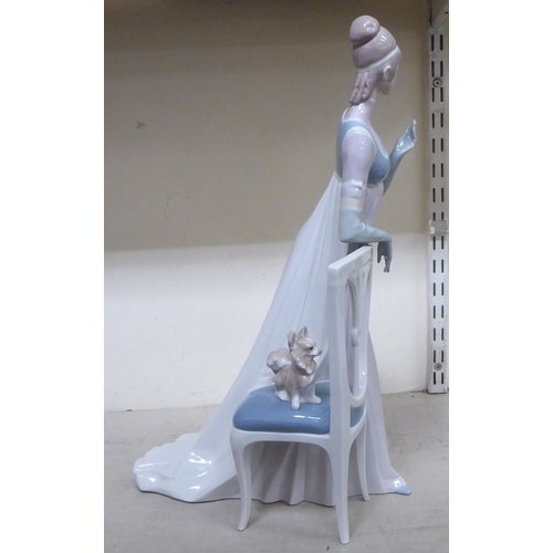 307 - A Lladro porcelain figure, a lady wearing a long gown, standing bedside a chair  model no.1276  19