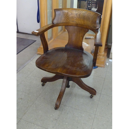 215 - An early 20thC oak framed round back desk chair with open arms and a solid seat, rotating and raised... 