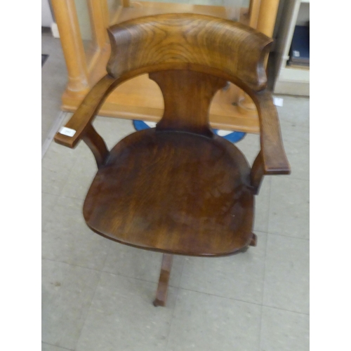 215 - An early 20thC oak framed round back desk chair with open arms and a solid seat, rotating and raised... 