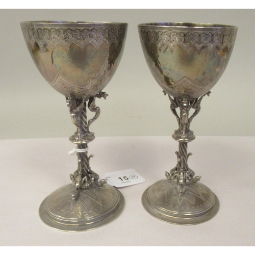 15 - A pair of late 19thC silver Gothic inspired goblets with uniformly engraved decoration, each ovoid s... 
