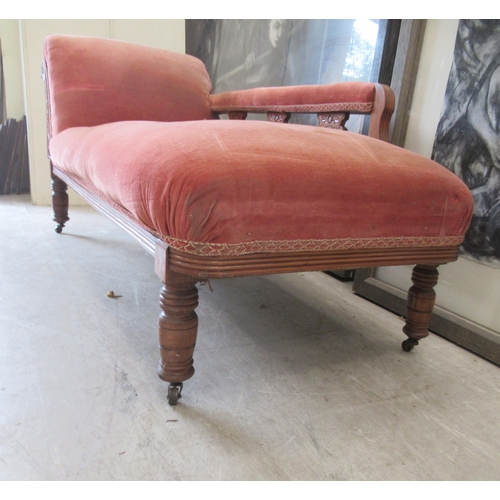 111 - A late Victorian walnut framed chaise longue, upholstered in a red fabric, raised on turned legs