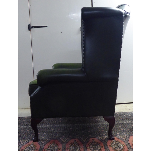 43 - A modern wingback armchair, stud and part button upholstered in green hide, raised on cabriole forel... 