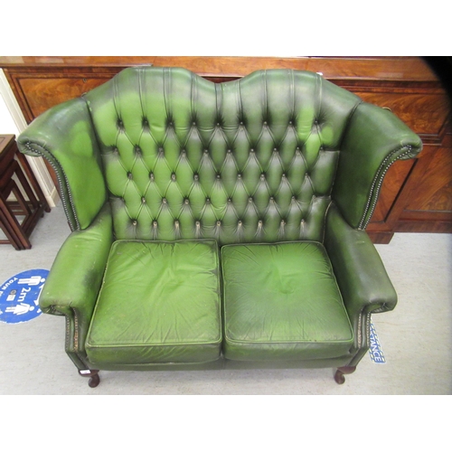 44 - A modern wingback settee, stud and part button upholstered in green hide, raised on cabriole foreleg... 