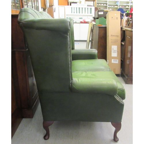 44 - A modern wingback settee, stud and part button upholstered in green hide, raised on cabriole foreleg... 