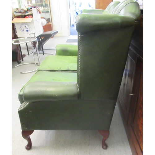 44 - A modern wingback settee, stud and part button upholstered in green hide, raised on cabriole foreleg... 