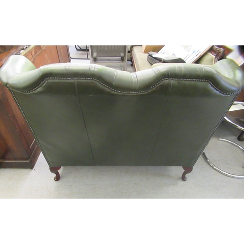 44 - A modern wingback settee, stud and part button upholstered in green hide, raised on cabriole foreleg... 