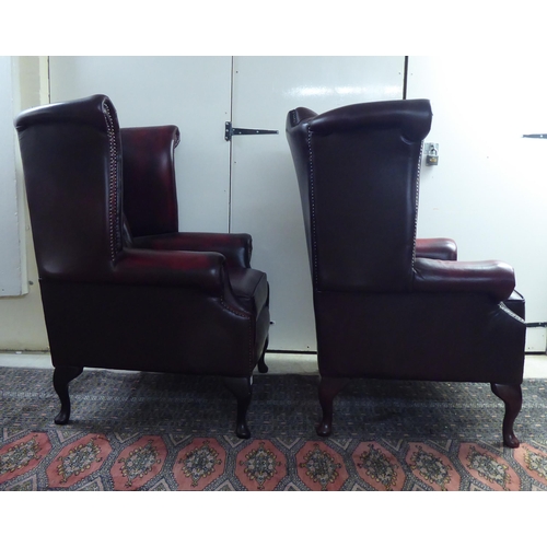 46 - A pair of modern wingback armchairs, stud and part button upholstered in oxblood coloured hide, rais... 