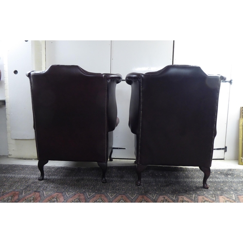 46 - A pair of modern wingback armchairs, stud and part button upholstered in oxblood coloured hide, rais... 