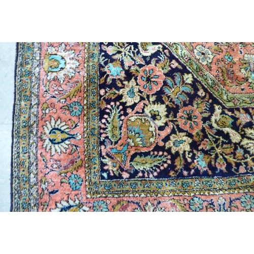 73 - A Persian woollen and silk rug, decorated with dense flora, on a peach, blue and green ground  56