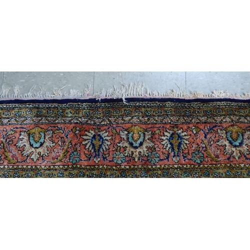 73 - A Persian woollen and silk rug, decorated with dense flora, on a peach, blue and green ground  56