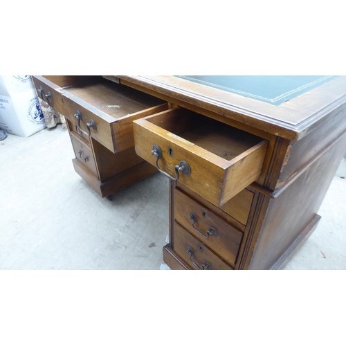 137 - An early 20thC oak nine drawer, twin pedestal desk, on a plinth and casters  30