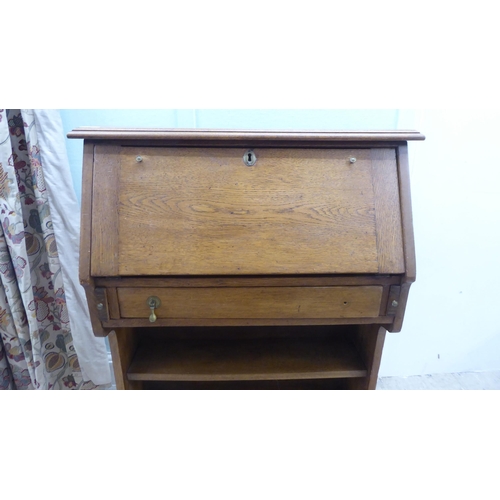 16 - An early 20thC light oak student's bureau with a fall flap, over two open shelves, raised on planked... 