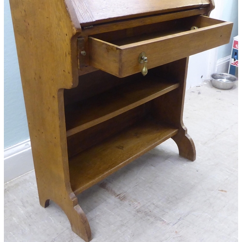 16 - An early 20thC light oak student's bureau with a fall flap, over two open shelves, raised on planked... 