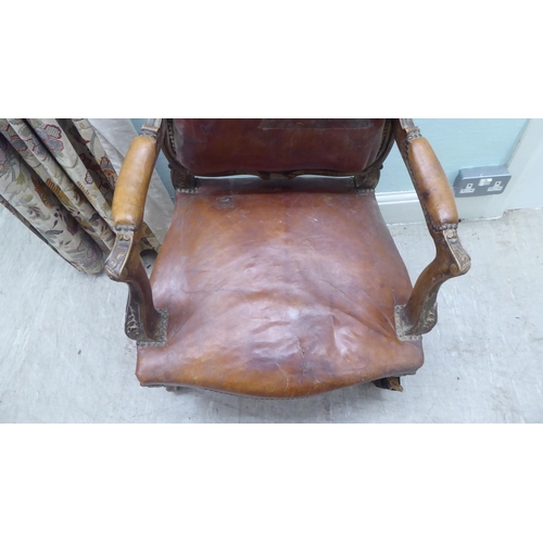 183 - A late 19thC Continental carved showwood framed open arm salon chair, stud upholstered in red hide, ... 