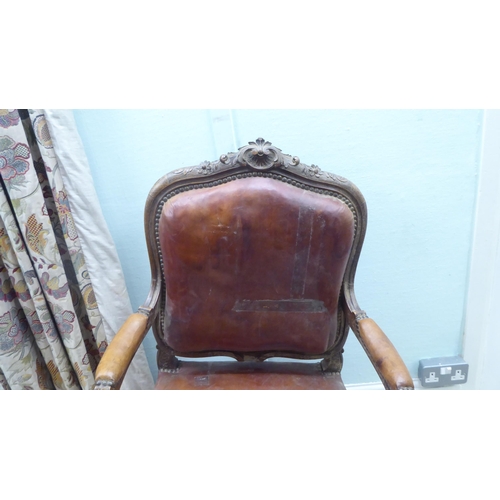 183 - A late 19thC Continental carved showwood framed open arm salon chair, stud upholstered in red hide, ... 