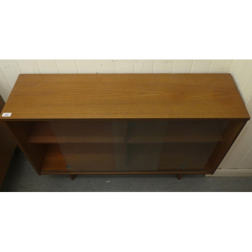 400 - A 1960s teak finished dwarf bookcase, the shelves enclosed by sliding doors, raised on block feet&nb... 