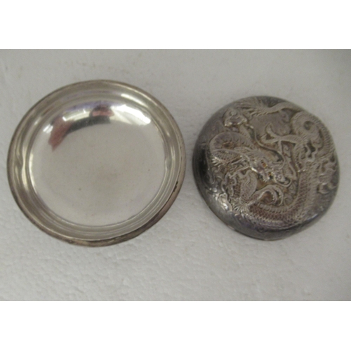 42 - An Oriental white metal circular tablet box, the cover cast with a dragon and inscribed on the under... 