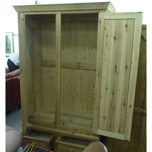 13 - A modern pine two part wardrobe with a pair of panelled doors, enclosing a hanging rail, over a thre... 