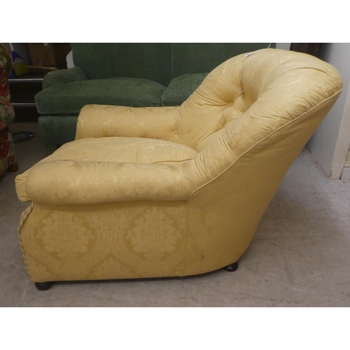 48 - An early 20thC and later gold floral patterned fabric, upholstered low, enclosed armchair, raised on... 