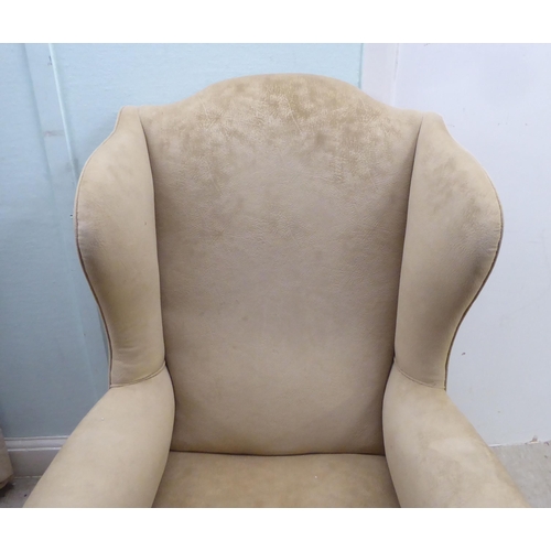 103 - An early 20thC Georgian style wingback armchair, upholstered in mushroom coloured fabric, raised on ... 