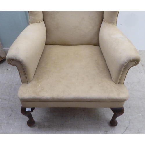 103 - An early 20thC Georgian style wingback armchair, upholstered in mushroom coloured fabric, raised on ... 