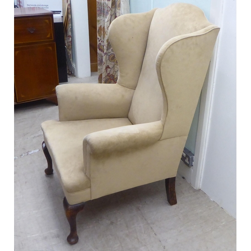 103 - An early 20thC Georgian style wingback armchair, upholstered in mushroom coloured fabric, raised on ... 