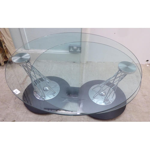 152 - A modern chromium plated steel wire framed eclipse type table, comprising two plate glass tops, rota... 