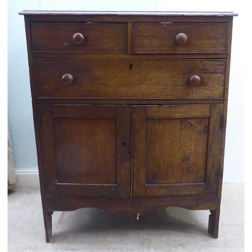 158 - An early 20thC oak cupboard, comprising two short/one long drawers, over a pair of panelled doors, r... 