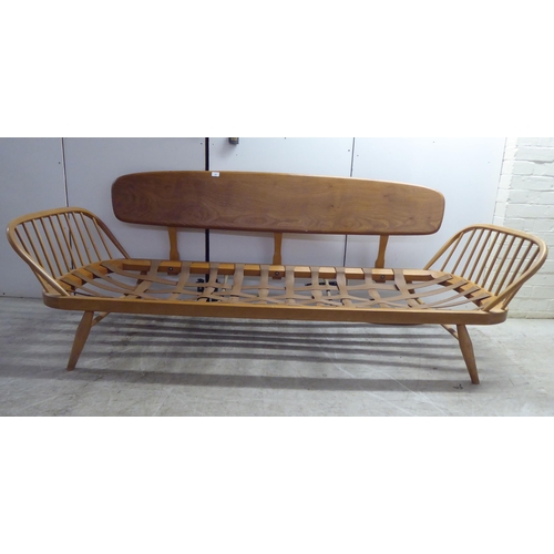 77 - An Ercol blonde elm and beech framed daybed with a solid surfboard back and low hoop and spindled ba... 