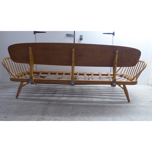 77 - An Ercol blonde elm and beech framed daybed with a solid surfboard back and low hoop and spindled ba... 