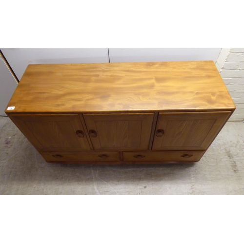 79 - An Ercol honey coloured elm sideboard, comprising three inline doors, enclosing a fitted interior, o... 