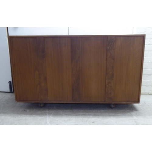 79 - An Ercol honey coloured elm sideboard, comprising three inline doors, enclosing a fitted interior, o... 