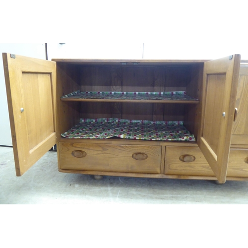 79 - An Ercol honey coloured elm sideboard, comprising three inline doors, enclosing a fitted interior, o... 