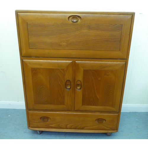 307 - A blonde Ercol elm side cabinet with a fall flap, over two cupboard doors and a long drawer, on a pl... 