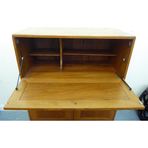 307 - A blonde Ercol elm side cabinet with a fall flap, over two cupboard doors and a long drawer, on a pl... 