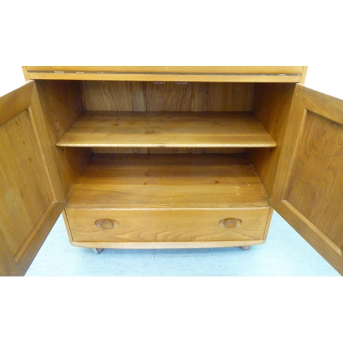 307 - A blonde Ercol elm side cabinet with a fall flap, over two cupboard doors and a long drawer, on a pl... 