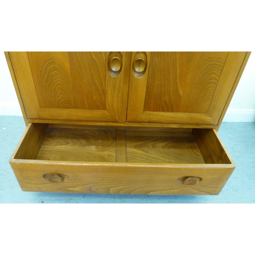 307 - A blonde Ercol elm side cabinet with a fall flap, over two cupboard doors and a long drawer, on a pl... 