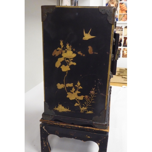 123 - A late 19th/early 20thC Japanese black lacquered and engraved metal mounted, two-part table cabinet,... 