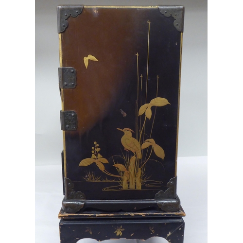 123 - A late 19th/early 20thC Japanese black lacquered and engraved metal mounted, two-part table cabinet,... 