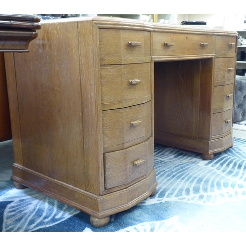 141 - An Art Deco period light oak nine drawer inverted breakfront twin pedestal desk with a maroon hide s... 