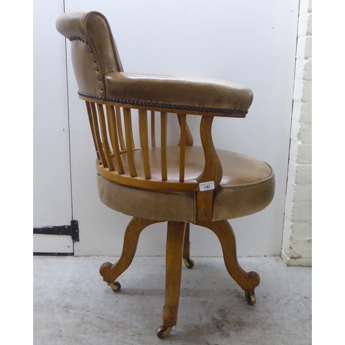 142 - An early 20thC light oak framed desk chair with a round back and square, vertical rails, upholstered... 