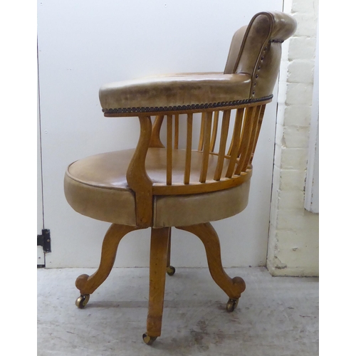 142 - An early 20thC light oak framed desk chair with a round back and square, vertical rails, upholstered... 