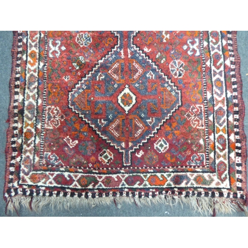 158 - A Persian rug, decorated with two diamond shaped motifs, bordered by stylised designs, on a red grou... 