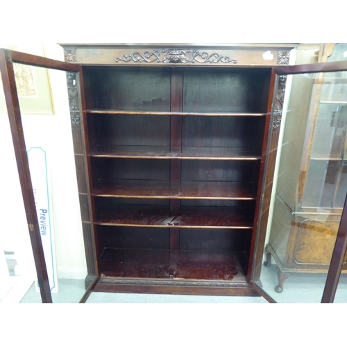 172 - A late Victorian mahogany bookcase with carved mask ornament and two glazed doors, on a plinth ... 