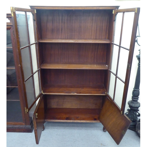 172 - A late Victorian mahogany bookcase with carved mask ornament and two glazed doors, on a plinth ... 