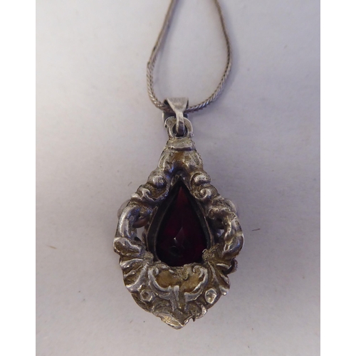 198 - A white metal pendant, set with a raised teardrop cut garnet, on a white metal chain  stamped 8... 