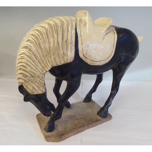 209 - In the manner of a Jang, black and cream coloured glazed pottery model, a standing horse, on a plint... 