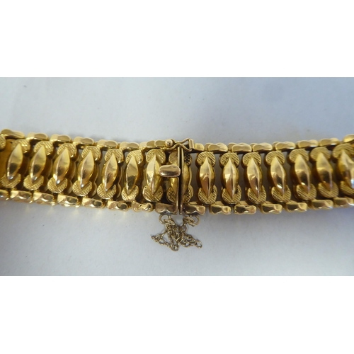 52 - An 18ct gold wide, flexible and engraved, open link bracelet, on a bayonet clasp with safety chain