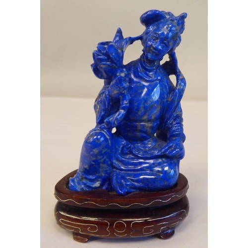 56 - An Oriental carved lapis lazuli kneeling figure, wearing traditional ceremonial costume, holding a l... 