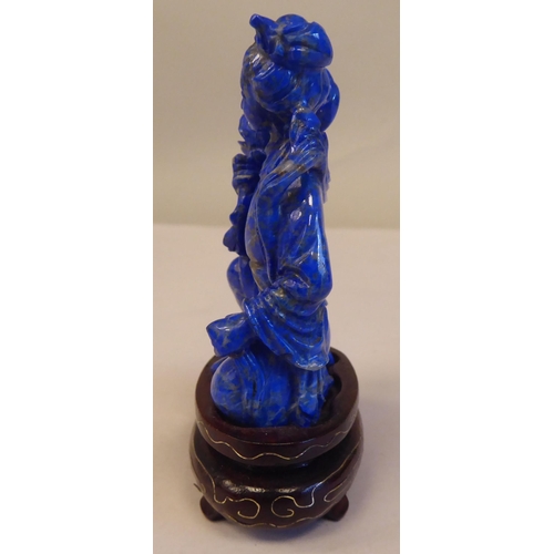 56 - An Oriental carved lapis lazuli kneeling figure, wearing traditional ceremonial costume, holding a l... 